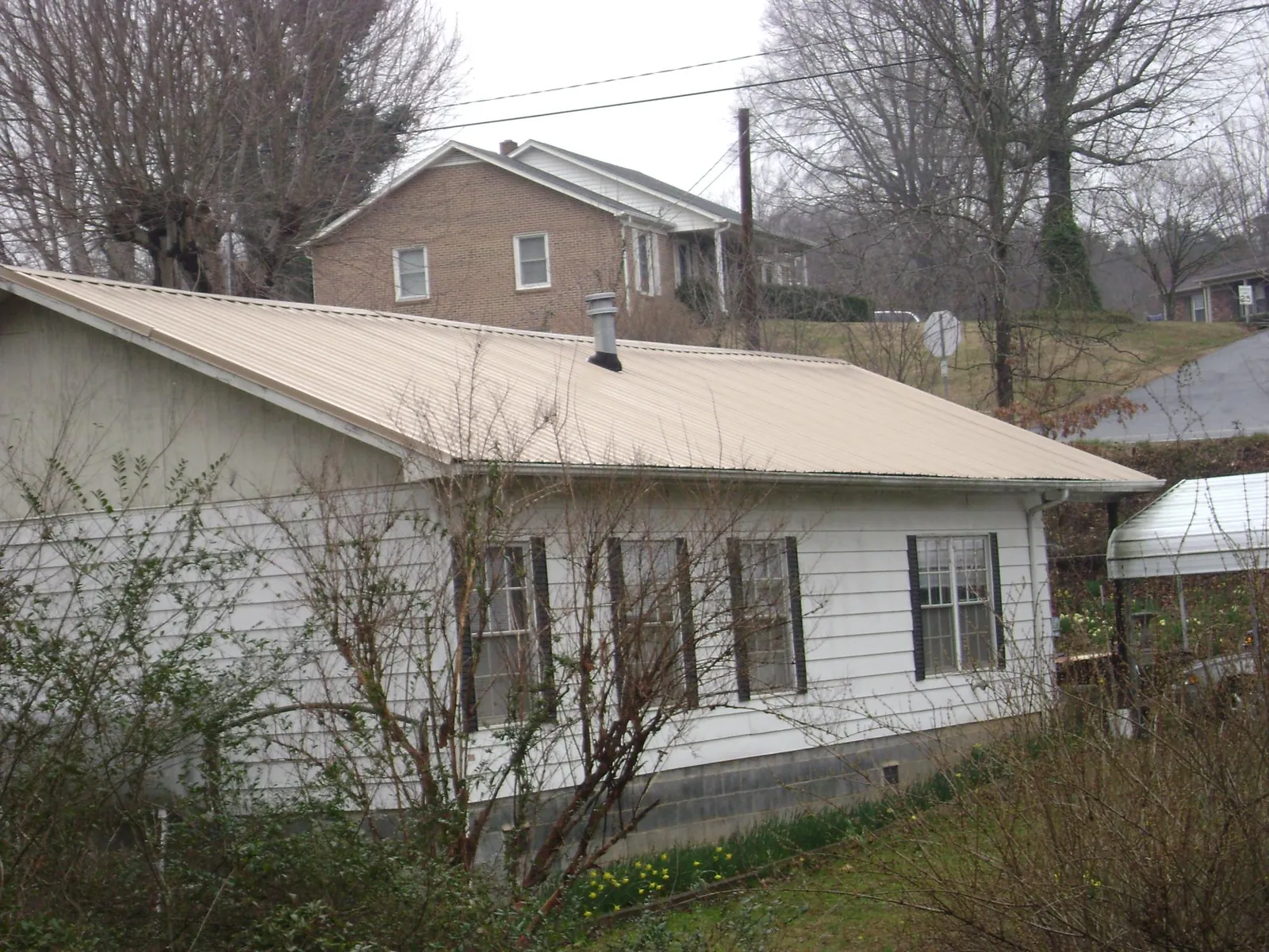 Tan metal roof on a white sided house set into a hillside — Commercial Roofing by Roofing Brothers in Taholah